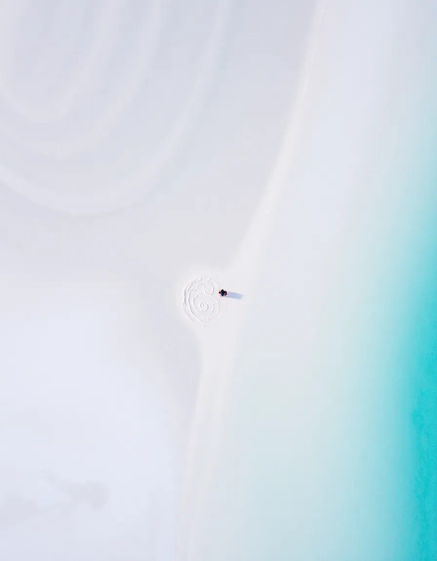 Aerial view of Hill Inlet’s swirling sands and aqua waters, with a tiny couple barely visible on a secluded patch of shore. The contrast between the white sand and blue water looks almost surreal.